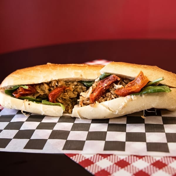 A large sub sandwich, cut in half, filled with meat, spinach, and sun-dried tomatoes.